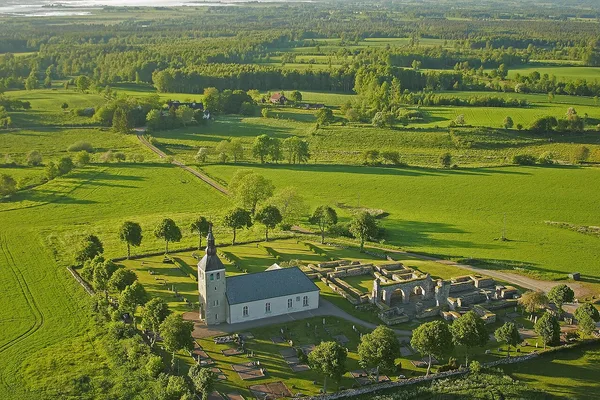 Flygfoto av vit kyrka med kyrkogård i grönt jordbrukslandskap