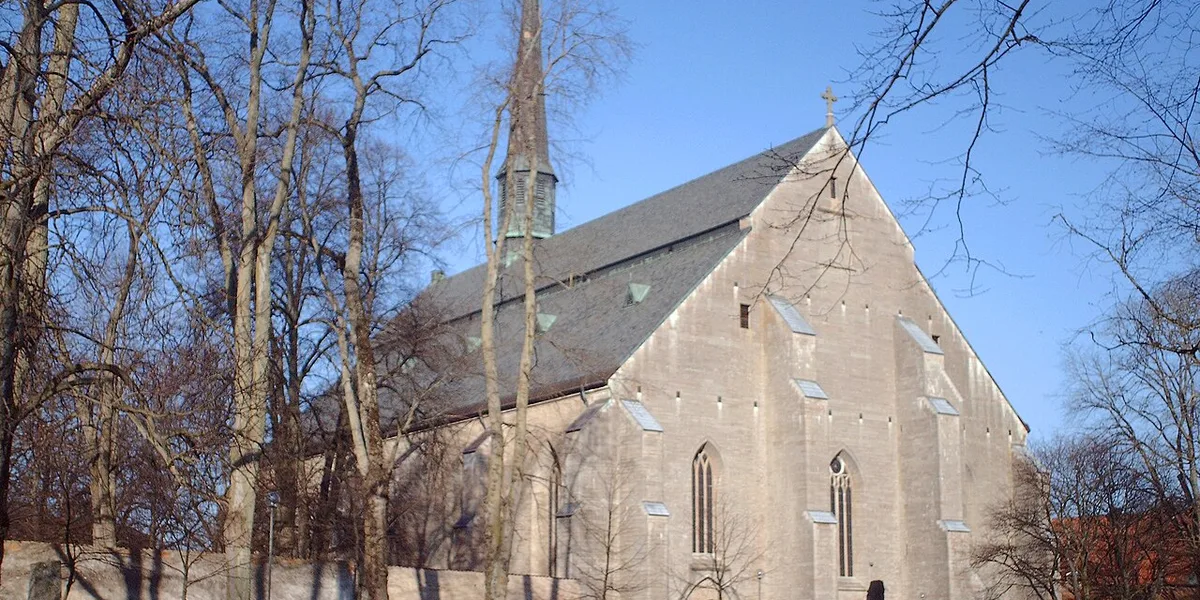 Medeltida stenkyrka med spetsigt tak omgiven av kala träd