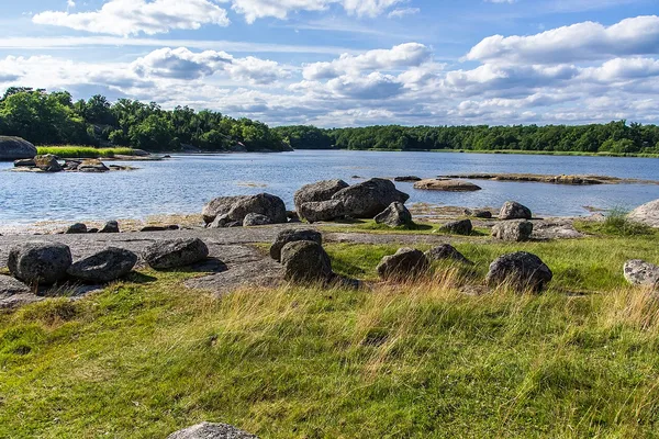 Klippig kust med stora stenar, gräs och stilla havsvik