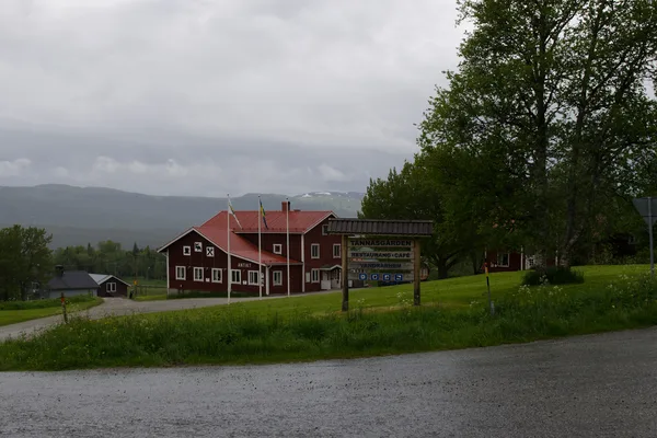 Röd fjällgård med skylt vid vägen, fjäll med snö i bakgrunden