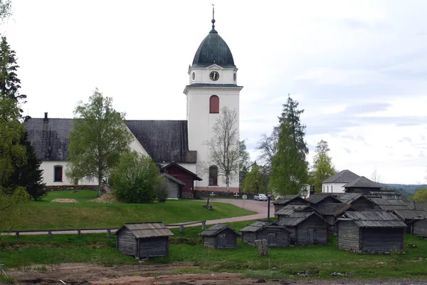 Vit kyrka med klocktorn och omgivande kyrkstugor i trä